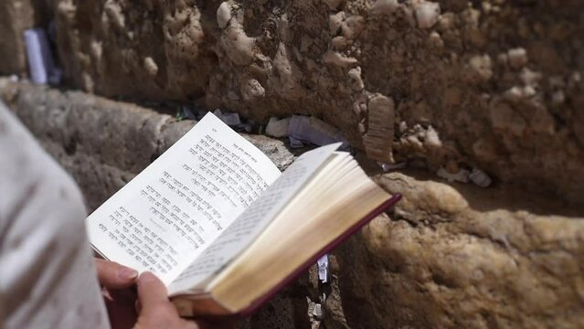 Open holy book - Torah in hands of praying woman near Wailing Wall in Jerusalem. People from different countries come to Israel and leave notes with prayers, dreams and requests to God on wall.