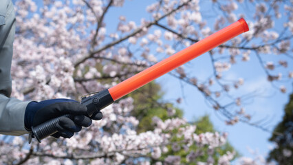 桜と作業服で誘導棒を持つ人｜建設業・警備業　入社イメージ
