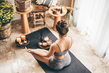 Young woman sitting in the lotus position on floor in a cozy boho room.