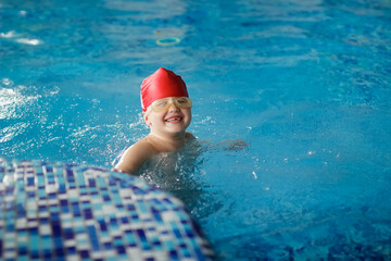A child in a cap and glasses swims dives in the pool