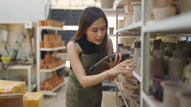 Asia female ceramist with apron hand arrange her clay sculp product on the shelf waiting for bake in oven,asian woman small business ceramic workshop owner smiling proud to present her new collection 