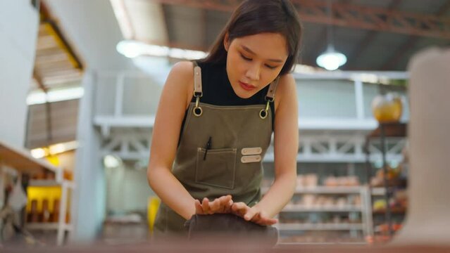 smiling asian female artist potters in aprons sculping clay ceramic product on working table in workshop. asia young female standing near hand makeing clay the art of pot making in factory