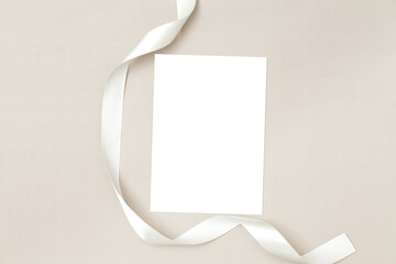 Wedding invitation or greeting card mockup with white satin ribbon on a beige background.