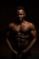 Fototapeta na wymiar Portrait of an African American man with a naked torso in a dark studio. Muscular guy.