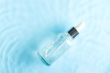Cosmetic spa medical skin care, bottle with serum, micellar toner and essence on blue water texture background with splashes. Flat lay, copy space.