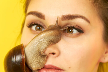 Cheerful young woman with a snail on her face on a yellow background