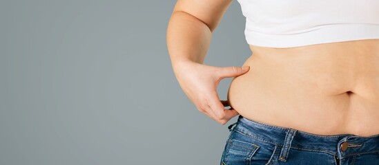 The slim girl with measure tape holds the skin on her stomach, showing fat deposits. Subcutaneous fat concept.