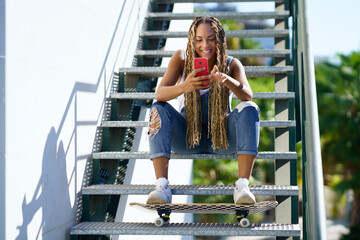 Cheerful black female skater browsing smartphone in city © javiindy
