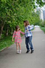 Fototapeta na wymiar Cute sibling sister girls with bow headband run and jump on sidewalk, happy kids walks