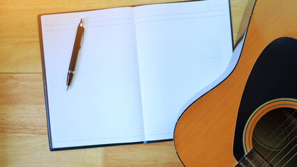The acoustic guitar was placed on the wooden floor beside a notebook and a black pen. songwriter...