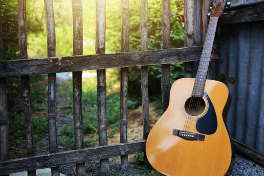 An acoustic guitar leans against an old wooden fence gate in the morning sun. left copy space.