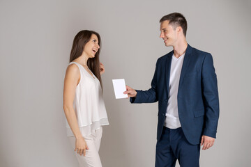 Business partner gives certificate to happy woman on gray background. Caucasian couple in business clothes, man gives beautiful girl a blank about winning the competition on a gray studio background