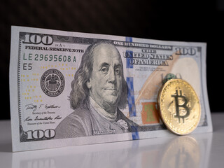 Gold coin Bitcoin on the background of 100 US dollars close-up. Cryptocurrency along with real currency