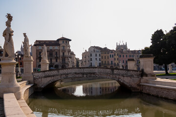 Naklejka premium Scenic view on bridge of Prato della Valle, square in the city of Padua, Veneto, Italy, Europe. Green island at center, Isola Memmia surrounded by canal bordered by two rings of statues. Reflection