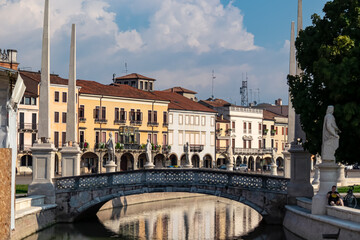 Fototapeta na wymiar Scenic view on bridge of Prato della Valle, square in the city of Padua, Veneto, Italy, Europe. Green island at center, Isola Memmia surrounded by canal bordered by two rings of statues. Reflection