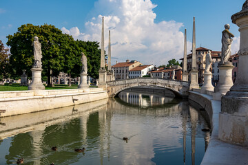 Obraz premium Scenic view on bridge of Prato della Valle, square in the city of Padua, Veneto, Italy, Europe. Green island at center, Isola Memmia surrounded by canal. Ducks are swimming in the water