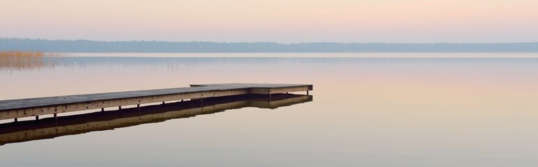 Forest lake (river) at sunrise. Wooden pier (boardwalk). Soft sunlight, mist, reflections on water....