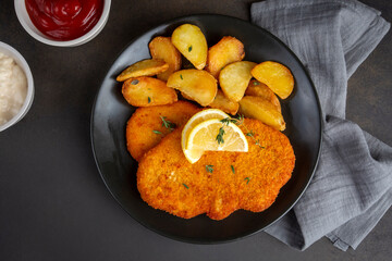 Chicken schnitzel with sauce, fried potatoes and lemon in a plate