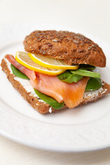 Closeup of homemade sandwich with slice of salmon, fresh lettuce leaf, cream cheese and lemon. Healthy food for family.