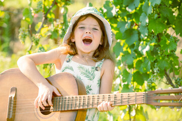 Excited child musician playing the guitar like a rockstar. Smiling child playing outdoors in summer.