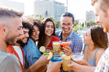 Group of happy multiracial friends having fun cheering and drinking cocktails while enjoying at summer party outdoor. Friendship and celebration concept - Focus on african curly woman