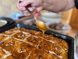 Woman holds a spoon with honey above pakhlava and pours it on the pastry. Baclava (or baklava) is Turkish, Greek, and Middle Eastern pastry of phyllo dough and nuts
