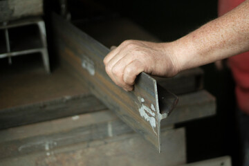 Worker with metal. The guy holds a steel part. Hard work in a metalworking workshop. Creation of steel construction.