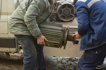 Men lift the engine. The engine from the elevator is in the hands of workers.