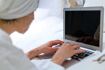 ホテルのベッドで寝そべってリモートワークしている女性　顔パック