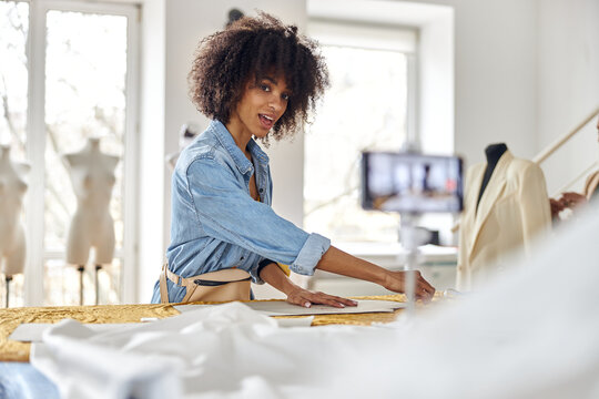 African-American woman draws pattern on fabric sheet shooting video for blog in workshop