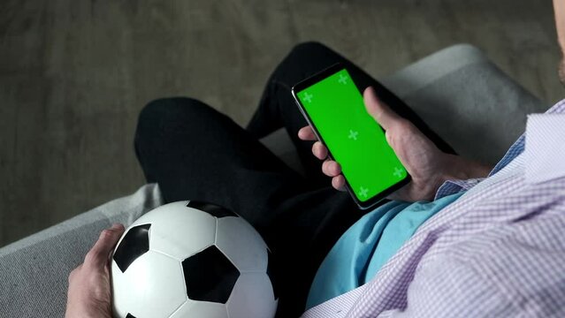 Football fan use smartphone at home with green chroma key Screen. Application At Home, Back View. Mobile App or advertisement.