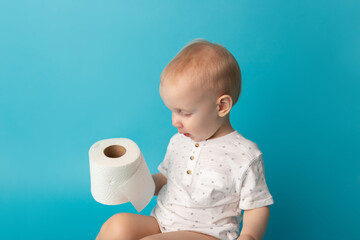 The child sits on the pot and unrolls toilet paper on color background. Concept to teach a child to go to the toilet and kids hygiene