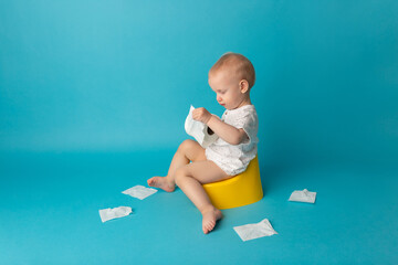 The child sits on the pot and unrolls toilet paper on color background. Concept to teach a child to...