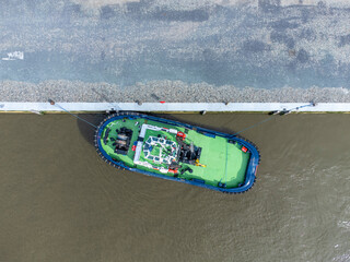 Green tugboat docked on the river Scheldt in Antwerp. Drone aerial top down view from above