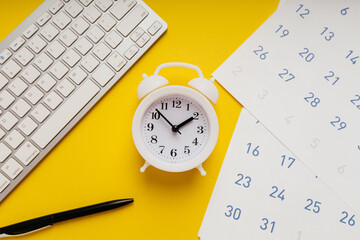 White keyboard, calendar and alarm clock on yellow background. Deadline and urgent tasks concept