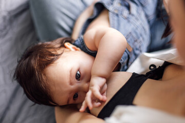 Obraz na płótnie Canvas Closeup portrait of breastfeeding little girl in denim baby romper, gray blurred background. Baby drink breast milk and get nutrients for healthy growth. Concept of maternal affection and childcare.