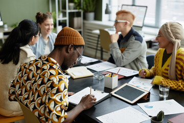 Back view at young black man taking notes in meeting with creative business team in office - Powered by Adobe