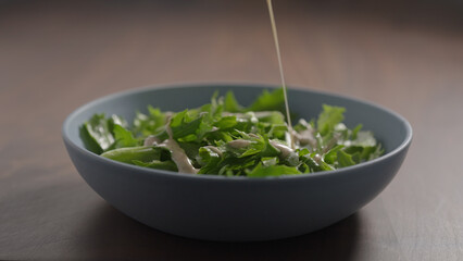making salad, pour dressing over frisee lettuce in blue bowl on wood table