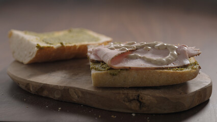 making sandwich, pour sauce over turkey slices on ciabatta on olive wood board