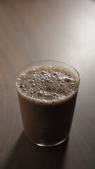 Vertical shot of chocolate milk or protein shake in tumbler glass on wood table
