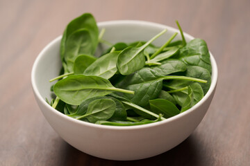 Fresh spinach leaves in white bowl on walnut wood table