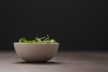 Fresh spinach leaves in white bowl on walnut wood table