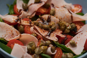 Salad with prosciutto cotto, cherry tomatoes and spinach in blue bowl closeup