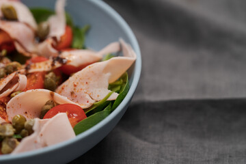 Salad with prosciutto cotto, cherry tomatoes and spinach in blue bowl