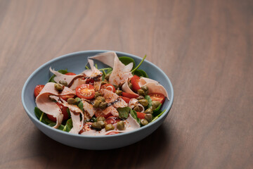 Salad with prosciutto cotto, cherry tomatoes and spinach in blue bowl