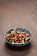 Salad with prosciutto cotto, cherry tomatoes and spinach in blue bowl