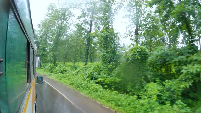 POV view of road from bus window with green trees and cloudy sky in rainy weather at Saputara in Dang district at Gujarat, India. Raindrop on lens. Road trip through mountains. Back to the road. 