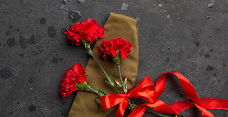 Victory Day, 9 May holiday concept. Carnation flowers, military cap with red ribbon on dark...