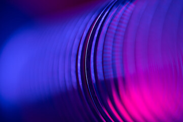 Closeup of coiled metal spring rings in a compressed state in pink and blue neon light. Macro...
