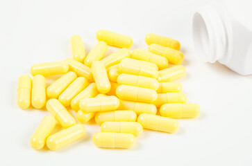 Yellow pharmaceutical medicine capsules over white background. White bottle with medical pills.